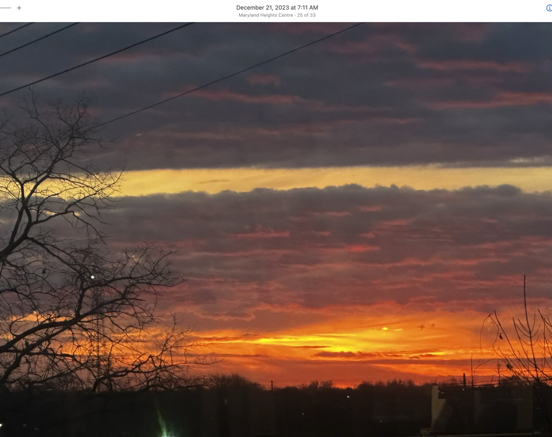 Narrow band of fiery light beneath dark morning clouds in Maryland Heights
