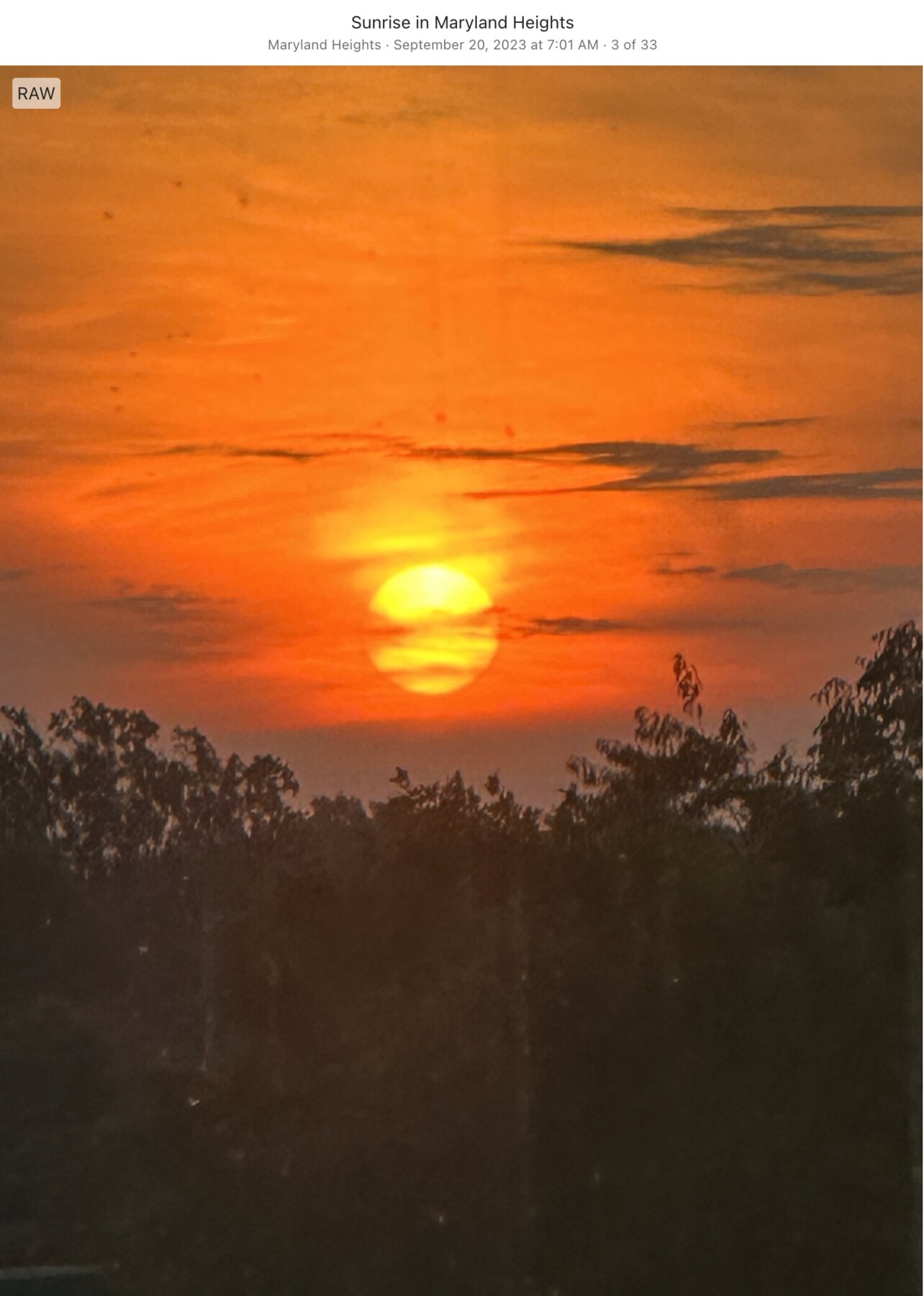 Deep orange sunrise above a dark treeline in Maryland Heights