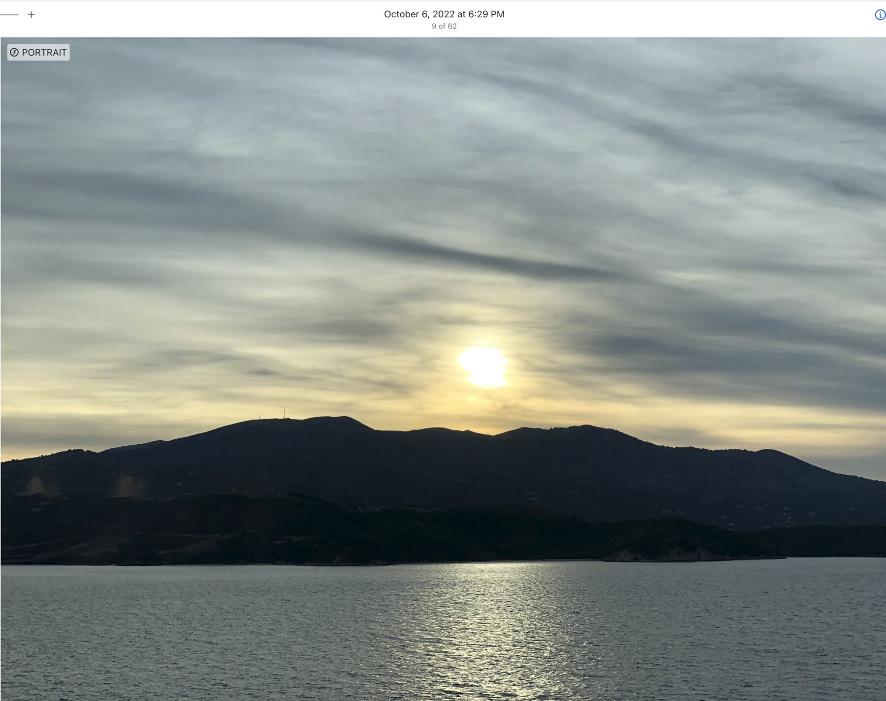 Pale sun above a dark island ridge and reflective water